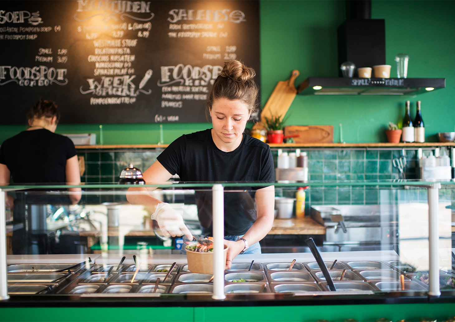 Medewerker van lokale foodspot bereidt verse salade achter buffet in kleurrijke horecazaak